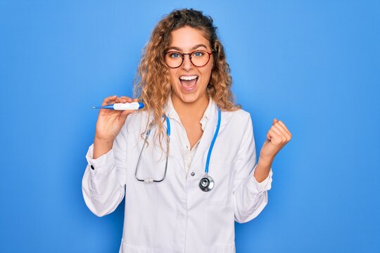 Young beautiful blonde doctor woman with blue eyes wearing stethoscope holding thermometer screaming proud and celebrating victory and success very excited, cheering emotion