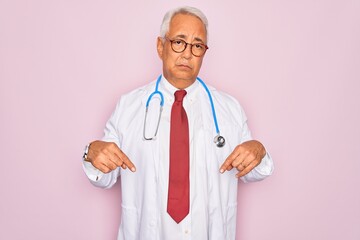 Middle age senior grey-haired doctor man wearing stethoscope and professional medical coat Pointing down looking sad and upset, indicating direction with fingers, unhappy and depressed.