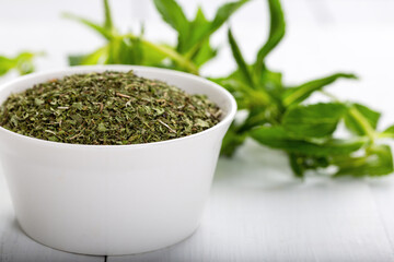 Dried peppermint in a white bowl and a bunch of fresh mint, on wooden background. Food background.