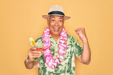 Middle age senior grey-haired man wearing summer hat and hawaiian lei drinking a cocktail screaming proud and celebrating victory and success very excited, cheering emotion