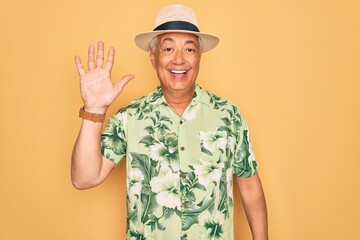 Middle age senior grey-haired man wearing summer hat and floral shirt on beach vacation showing and pointing up with fingers number five while smiling confident and happy.