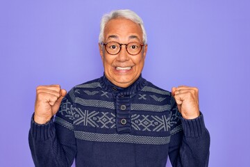 Middle age senior grey-haired man wearing glasses and winter sweater over purple background celebrating surprised and amazed for success with arms raised and open eyes. Winner concept.