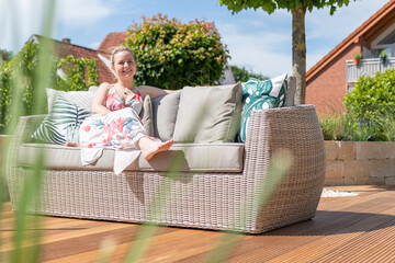 Attractive blonde woman and dog relaxing on a wooden terrace with green garden and modern outdoor...