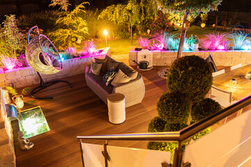 Colourful garden lighting and modern wooden terrace with outdoor furniture