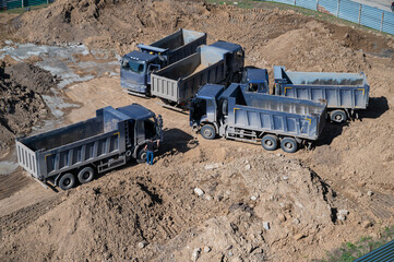 Aerial top view of several dump trucks unloading sand at a construction site. Industrial panorama.