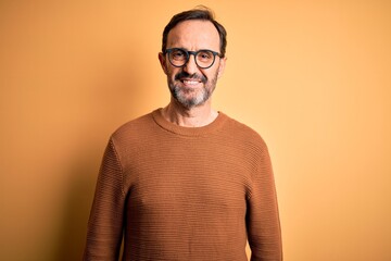 Middle age hoary man wearing brown sweater and glasses over isolated yellow background with a happy...