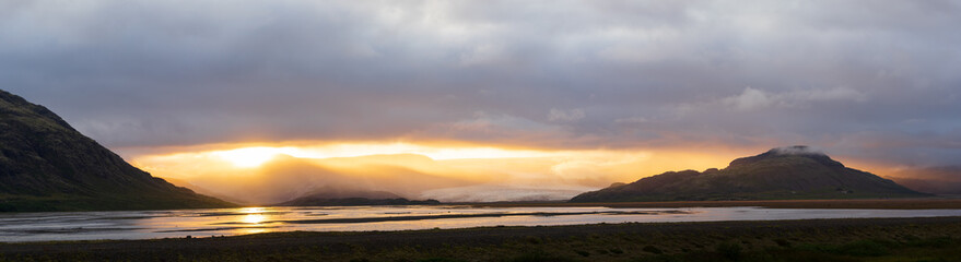 Naklejka premium Sun breaking through clouds between mountains, mystical sunset in Iceland