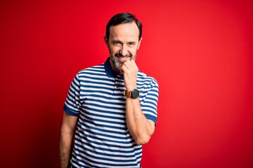 Middle age hoary man wearing casual striped polo standing over isolated red background looking confident at the camera with smile with crossed arms and hand raised on chin. Thinking positive.
