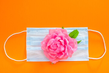 Pink flower on a medical mask. The concept of preserving health during a pandemic. Fighting the...