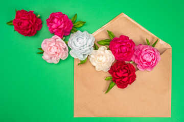 Bright flowers fly out of the brown envelope. A romantic message. Holiday greetings. Nice message. Bright peonies on a green background with space for text.
