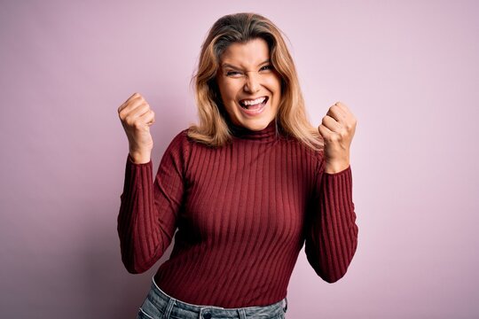 Young beautiful blonde woman wearing casual sweater over isolated pink background celebrating surprised and amazed for success with arms raised and open eyes. Winner concept.
