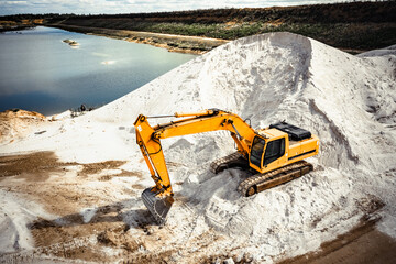 yellow and orange excavator, bulldozer, tractor in a sand pit removed from the air dig with a bucket