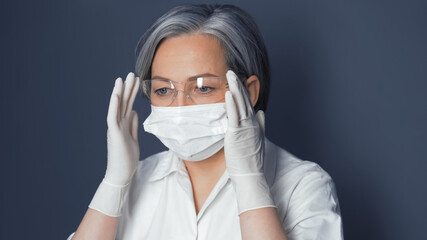 Doctor in uniform adjusts safety glasses. Cute Caucasian woman wearing protective mask and...