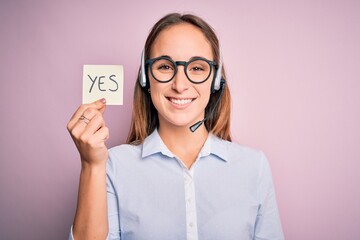 Beautiful call center agent woman working using headset holding reminder with yes message with a...