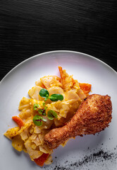 Roasted chicken leg and vegetables in white plate on black wooden table background