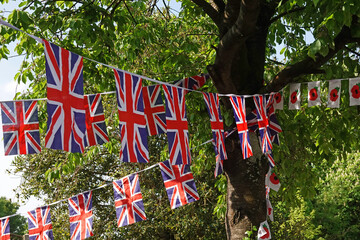 Union flag and poppy flag bunting hanging in the shade of a tree on a village green in the UK