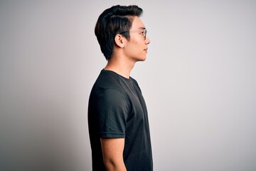 Obraz premium Young handsome chinese man wearing black t-shirt and glasses over white background looking to side, relax profile pose with natural face with confident smile.