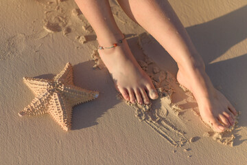 Fototapeta na wymiar Women's feet and starfish on yellow sand.