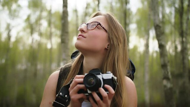 Young caucasian woman traveler with backpack and vintage camera surrounded by trees. Portrait slow motion shot.