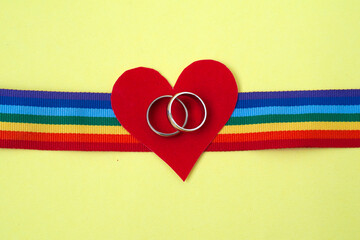 pair of golden wedding rings on LGBT rainbow ribbon on yellow background