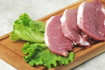 raw pork steak - pork neck - with lettuce leaves on a wooden Board