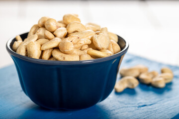 Cashew in a ceramic bowl on a white wooden background.