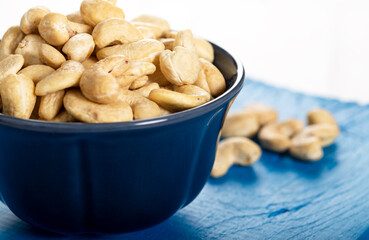 Cashew in a ceramic bowl on a white wooden background.