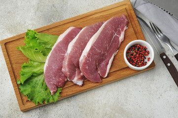 raw pork steak - pork neck - with lettuce leaves on a wooden Board