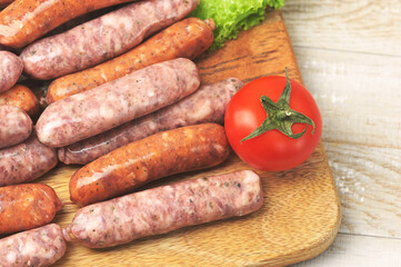 raw grilled sausages on a wooden round Board with tomatoes