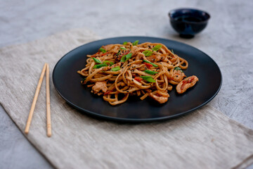 Asian udon noodles with chicken vegetables and teriyaki sauce with chopsticks and a linen napkin on...