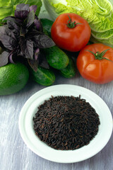 Black rice in a white plate with vegetables on a gray background.