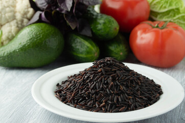 Black rice on a white plate on a background of vegetables.