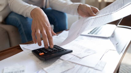 Close up of young woman manage home family expenditures, calculate on machine, paying bills taxes...