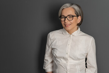 Intelligent middle aged woman with glasses smiling charmingly while looking at copy space on the...