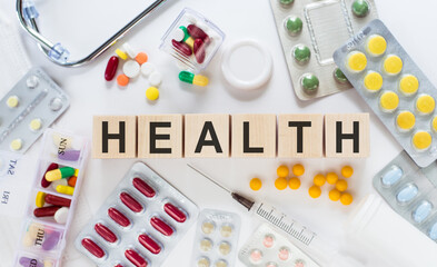 HEALTH word written on wood block. Health text on table with with medicines, pills, stethoscope. Medicine concept