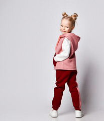 Little blonde model with buns hairstyle, in colorful tracksuit, sneakers. Smiling, performing exercises, posing isolated on white