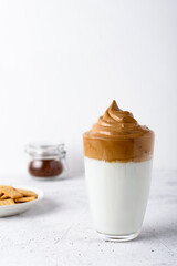 Homemade cold Dalgona coffee in a tall transparent glass with crackers on a light background. Trendy Korean coffee drink with foamed instant coffee and milk. Copy space from above.