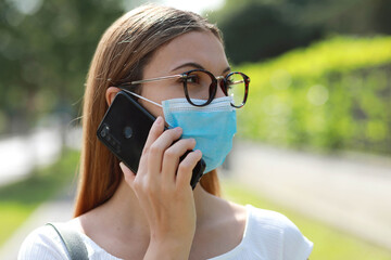 Pensive business woman talking on smart phone using surgical mask avoiding coronavirus in city...