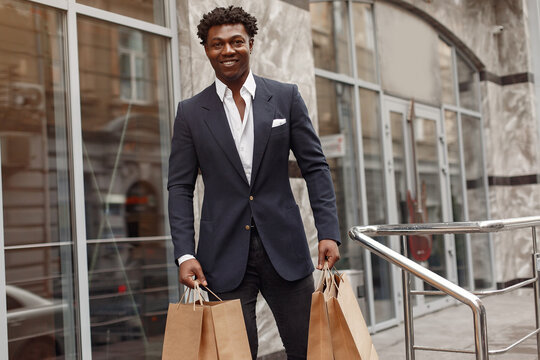 Black man in a city. Guy with shopping bags. Man in a black suit;