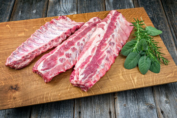 Raw pork spare loin ribs St Louis cut offered with herbs as closeup on a wooden board