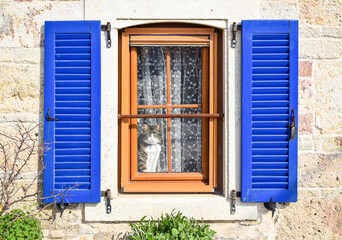 Obraz na płótnie Canvas A remarkable window with blue shutters of the stone-walled house. The cat is watching the street in front of the window.