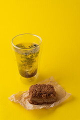 A tall glass of buckwheat tea and medovik cake on bright yellow studio background