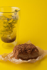 A tall glass of buckwheat tea and medovik cake on bright yellow studio background