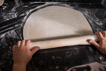 Top view of woman hands kneading the dough with wooden stick to preparing pizza or pide or pita bread that Turkish style of dumpling