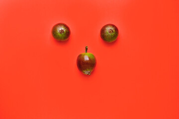 small three apples isolated on a red background, laid out in the form of a face.