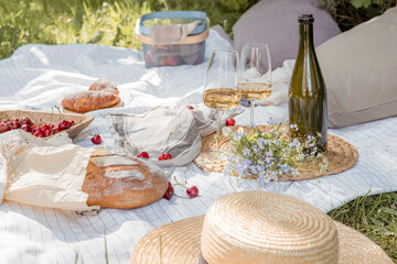Aesthetic picnic outdoors with wine glasses bread berries and flowers. Rustic picnic with neutral...