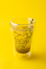 A tall glass of buckwheat tea with rosemary on minimalist bright yellow background, close up