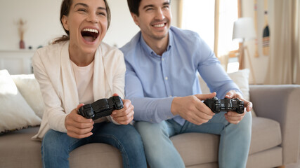 Close up of excited young man and woman sit on sofa have fun play video games together, overjoyed couple gamers relax enjoy console at home, entertainment concept