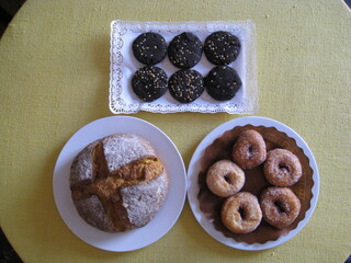 productos de distintas harinas, galletas algarroba, rosquillas trigo, hogaza de pan de maíz sobre tela amarilla. Panadería y repostería artesana, ecológica. Platos unidos en triángulo
