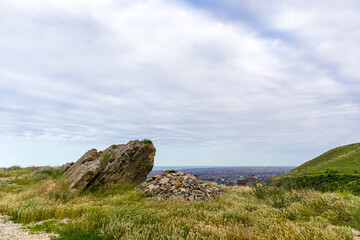 Big stone on the mountain above the city with cloudy sky background.